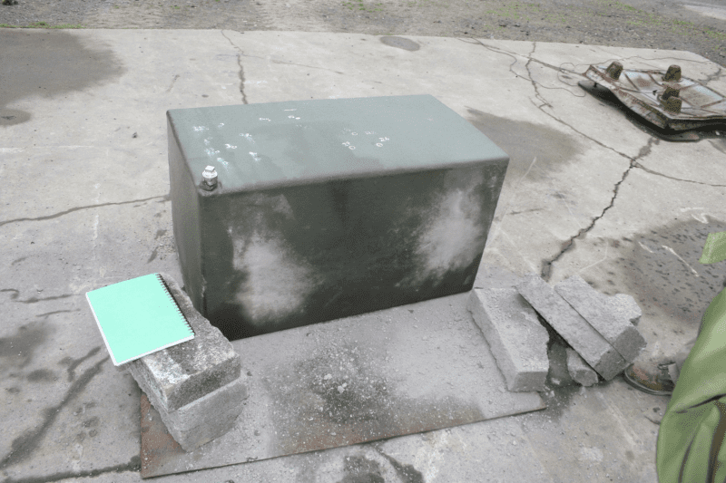 A large metal box on concrete, offering fuel tank protection, surrounded by breeze blocks.