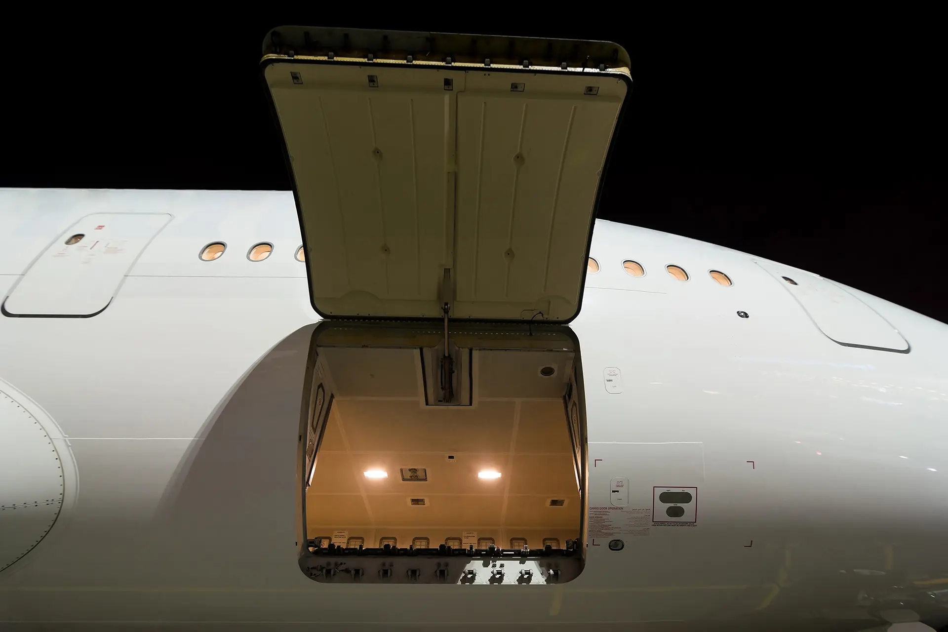 Cargo-Bay Open cargo door of an airplane at night, revealing the lit interior of the cargo hold.