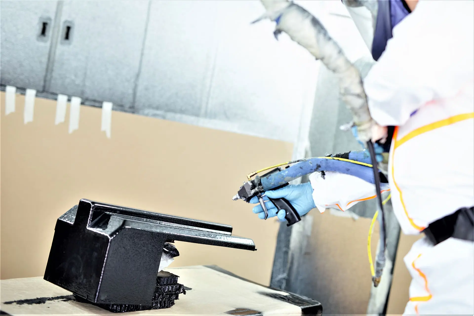 Coating-and-Painting-Retouched Person in protective gear spray-painting a black object in a workshop or industrial setting.