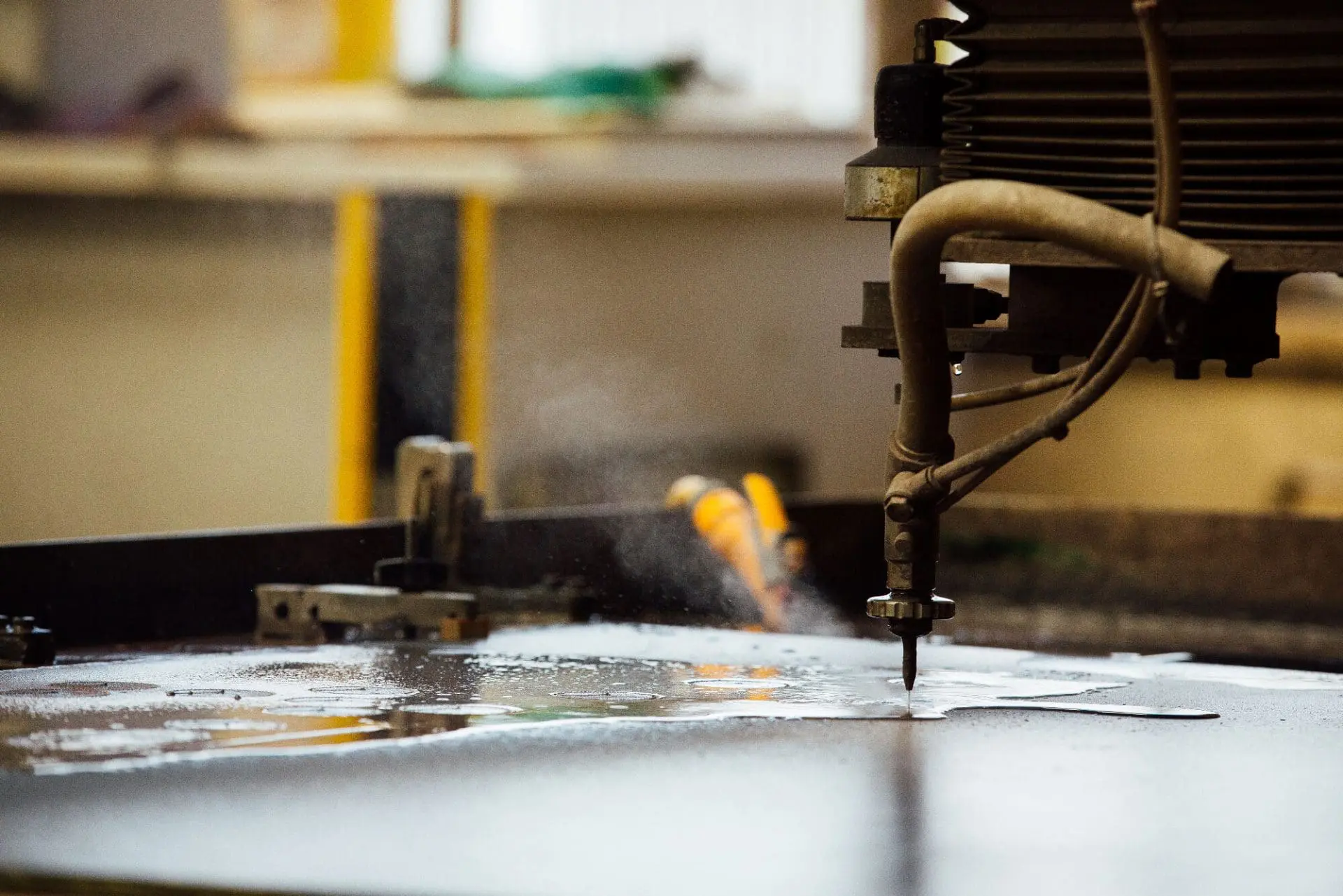 Permali-Machine A water jet cutting machine slices through a metal sheet, spraying water and mist in a workshop.