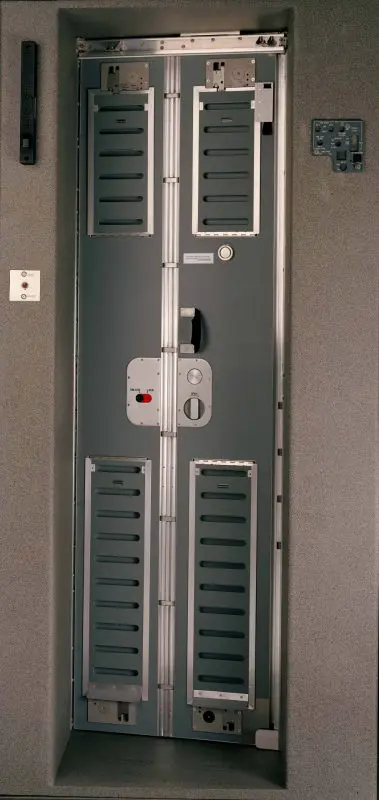 cockpit-door-379x800 A metal door with vents and control panels, set into a gray wall, possibly in an industrial setting.