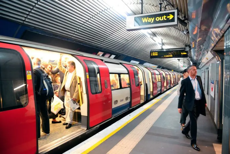 Commuters board and exit a London Underground train at a busy station with a Way out sign above.