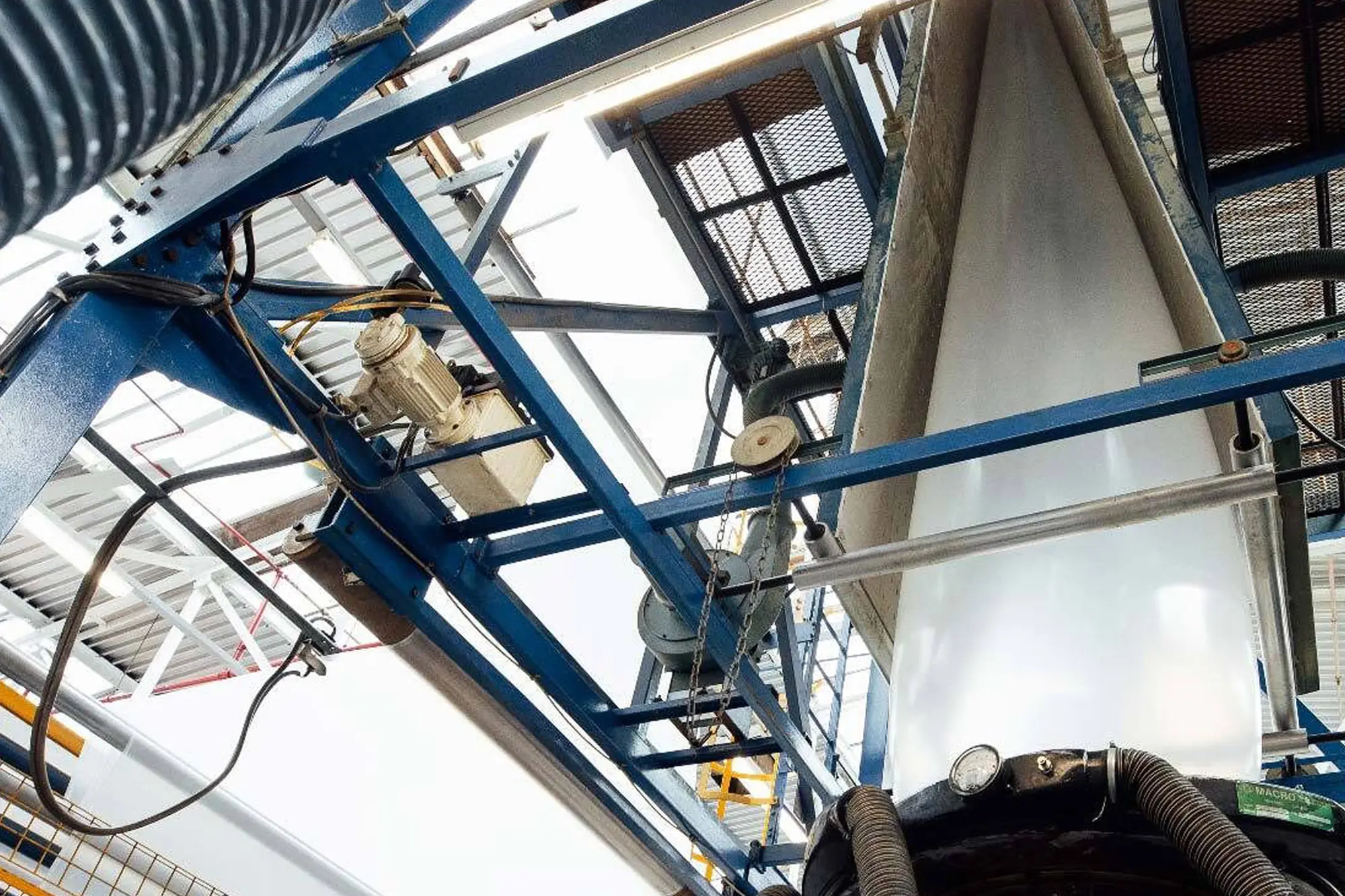 TUFSHIELD Industrial machinery with blue metal framework and pipes processing a large vertical sheet of plastic.