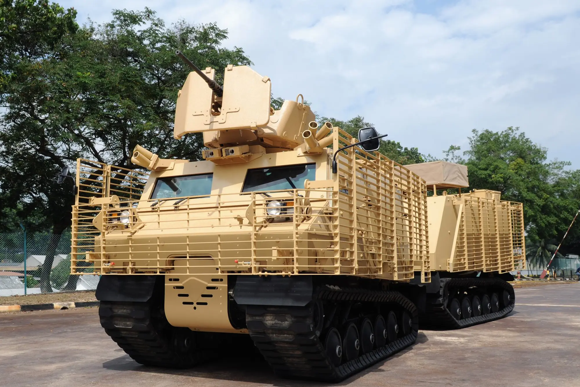 WATERHIG2 Tan armored military vehicle with tracks and grille armor parked outdoors on a paved surface.
