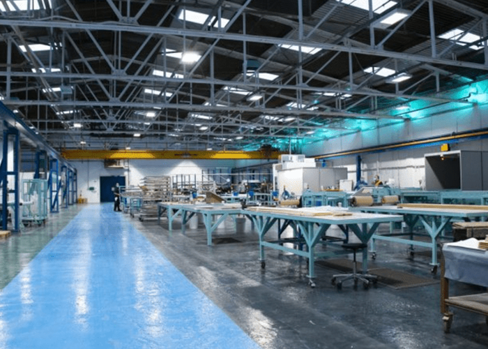 Spacious, well-lit factory interior with workbenches, machinery, and a blue walkway on the floor.