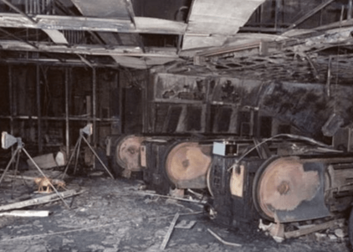 Three burnt slot machines in a heavily fire-damaged, debris-filled casino interior.
