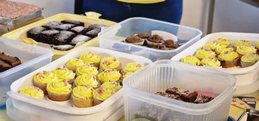 Assorted cupcakes and brownies in plastic containers on a table, ready to be served or sold.