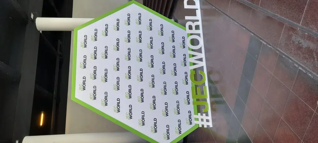 JEC-2025-3 A hexagonal JEC World display with a #JECWORLD hashtag in front, set indoors near stairs.