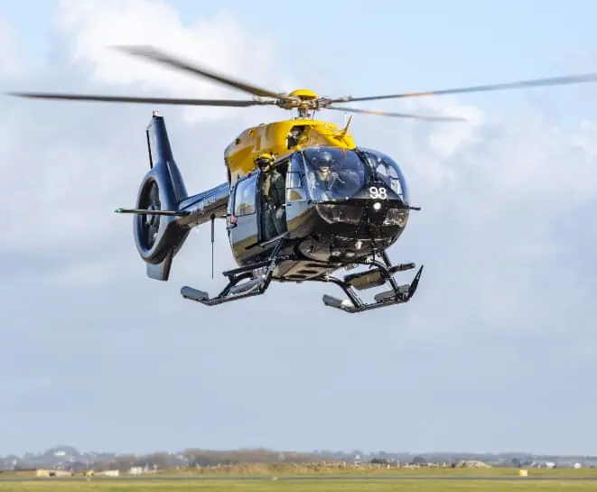 A black and yellow helicopter with number 98 hovers above a grassy, tactical composite flooring.