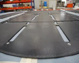 Close-up of Tactical Hard-Flooring black metal panels with slots and screws in a workshop.