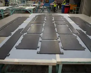 Large black tactical hard-flooring plates laid out on a workbench in an industrial workshop.
