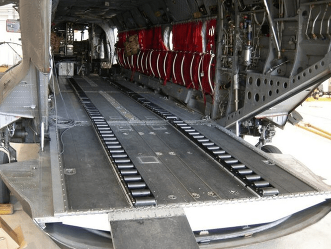 1.png-2-800×602 (1) Interior of a military cargo aircraft with a ramp lowered and seats folded along the sides.