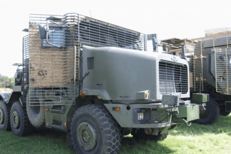 HETatDvD-800x600 Military truck with protective cage armor parked on grass in daylight.
