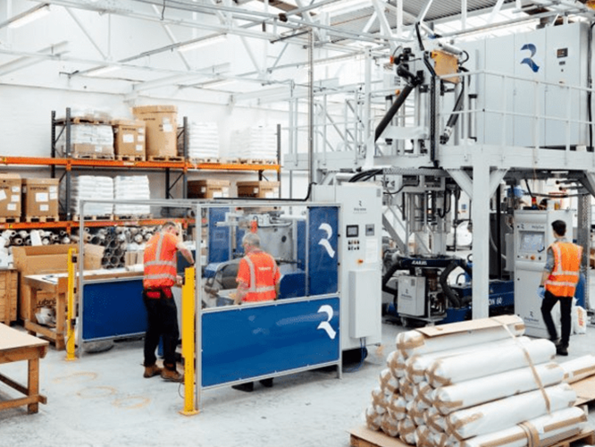Permali-Shoot-Proofs-024-e1591608687741-800×468 Three workers in safety vests operate machinery in a bright, organized industrial warehouse with stacked supplies.