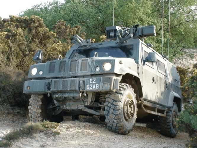 panther1-800×600 A military armored vehicle with rugged tires drives on a dirt path through a wooded area.