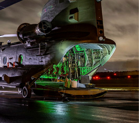 Nighttime view of an open military cargo aircraft with green-lit interior on a wet runway.