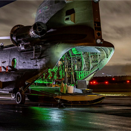 Nighttime view of an open military cargo aircraft with green-lit interior on a wet runway.