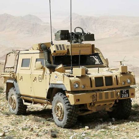Armored military vehicle parked on rocky terrain with desert mountains in the background.