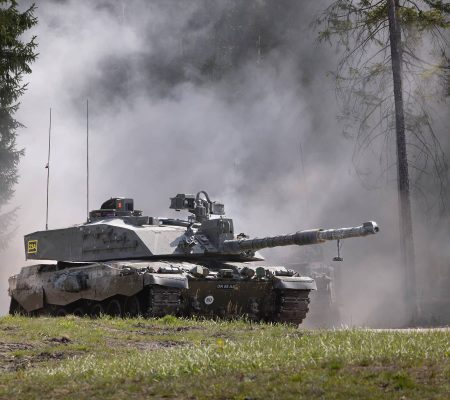 Challenger 2 - VCOPS-20250513-0043-Ex Hedgehog-1084 A military tank moves through a forested area with smoke rising around it.