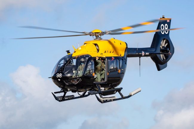 An Airbus H145M with number 98 soars in a partly cloudy sky, yellow and black in colour.