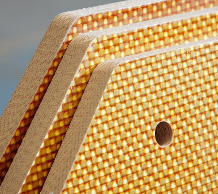 Aramid (2) Close-up of stacked textured yellow boards with rounded corners and a hole in one board.